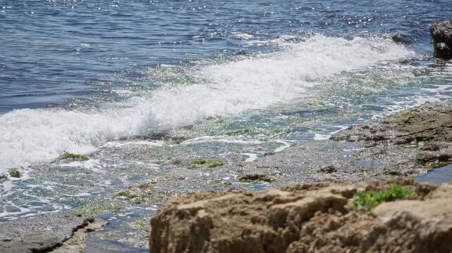 Serene mediterranean coastal scene with clear blue sea, sunlit waves breaking on rocky shore, showcasing nature's beauty during a sunny day outdoors.