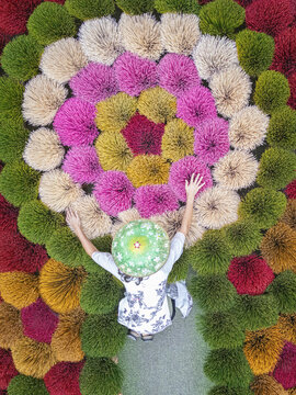 Aerial view of a person lying beneath a mandala-like display of vibrant, multi-colored floral arrangements, their arms outstretched in awe, Hanoi, Vietnam.