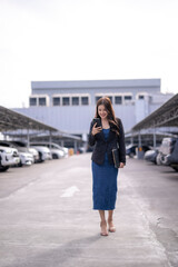 Obraz premium Asian businesswoman walking in parking lot using smartphone