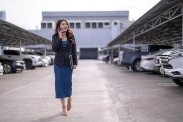 Fototapeta premium Asian businesswoman talking on phone walking in parking lot