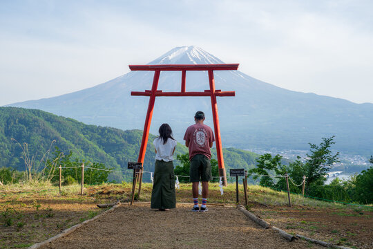 View of a couple framed by a vibrant red torii gate, gazing at majestic Mount Fuji against a clear sky, a serene tableau of nature and culture, Fujikawaguchiko, Yamanashi, Japan.