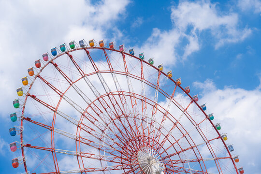 View of a vibrant ferris wheel in Odaba with colorful cars stands out against the bright blue sky dotted with fluffy white clouds, Tokyo, Tokyo, Japan.