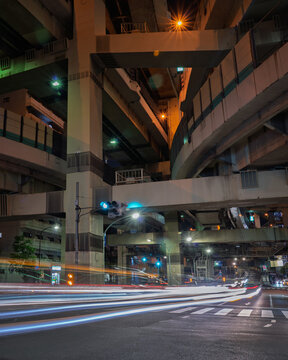 View of a complex web of elevated roads and bridges intertwining above a city street with light trails streaking across the asphalt, Shuto Expressway, Tokyo, Japan.