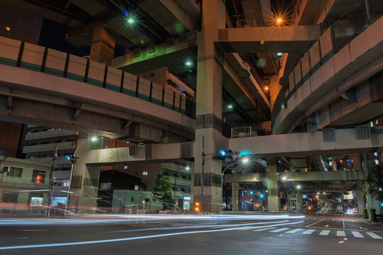 View of a complex network of elevated highways intertwines above a quiet street, with streaks of light painting the asphalt in the vibrant night, Shuto Expressway, Tokyo, Japan.
