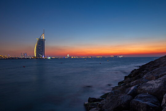 View of the iconic Burj Al Arab Jumeirah hotel illuminated against the fading sunset sky, casting a golden glow on the Arabian Gulf, Umm Suqeim Third, Dubai, United Arab Emirates.