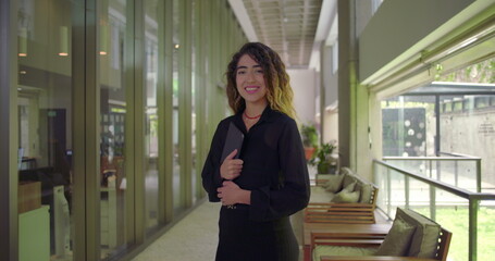 Fototapeta premium Young woman smiling in full body portrait while holding tablet, standing in office hallway, confident and approachable in modern business environment
