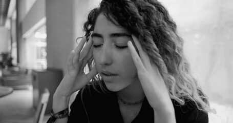 Young woman with eyes closed and fingers on temples, stressed and emotionally drained, monochrome image representing workplace burnout and mental health challenges