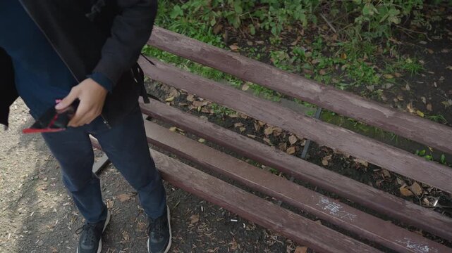 caucasian man prepping drone controller on bench. standing checks smartphone, lifts black backpack from bench, straps headphones around neck, powers compact remote, sits and adjusts sticks