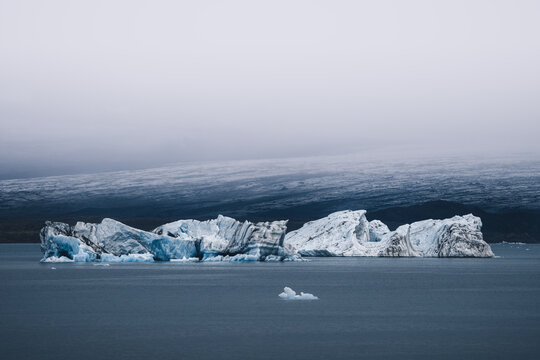 View of glistening icebergs contrasting with the calm, dark water of J&Atilde;&para;kuls&Atilde;&iexcl;rl&Atilde;&sup3;n Lagoon, under a muted sky creating a serene yet stark landscape, Vatnaj&Atilde;&para;kull National Park, South Iceland, Iceland.