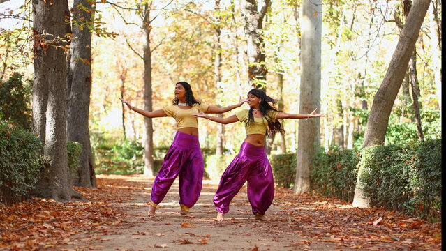 Two young women performing indian dance in autumn park
