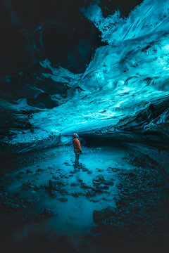 View of a person standing in a pool of water inside an ice cave, with blue ice formations overhead, creating a surreal and ethereal atmosphere, Vatnaj&Atilde;&para;kull National Park, South Iceland, Iceland.