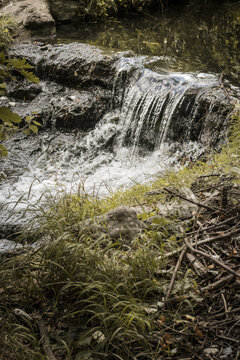 View of cascading water flowing over rocks amidst lush green grass and scattered branches, creating a serene, natural scene, Paris, &Atilde;Žle-de-France, France.