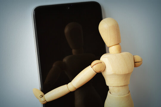 Wooden mannequin looking at his reflection in a smartphone screen - Concept of identity, self-perception and social media