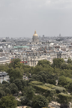View of Parisian rooftops and lush green trees stretch toward the golden dome of Les Invalides under a soft sky, Paris, &Atilde;Žle-de-France, France.