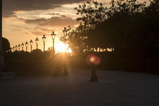 View of a line of vintage streetlights silhouetted against a vibrant sunset, casting long shadows across the pathway, Paris, &Atilde;Žle-de-France, France.