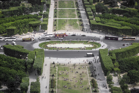 View of vibrant green trees and open spaces surrounding a bustling roundabout with buses and people, contrasting with the city, Paris, &Atilde;Žle-de-France, France.