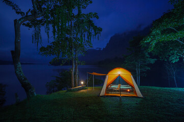 A tent glowing at night in a forest campsite surrounded by trees and nature during a peaceful outdoor camping adventure