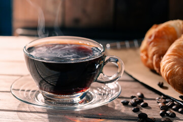 A close-up image of hot coffee in a mug with bread on a table, in the morning light, creating a warm atmosphere.