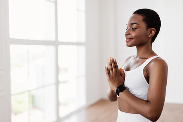 Fototapeta premium Keep Calm, Meditation And Healthy Lifestyle. Portrait of attractive smiling young black lady holding hands in prayer pose, keeping palms together, breathing and meditating, free copy space