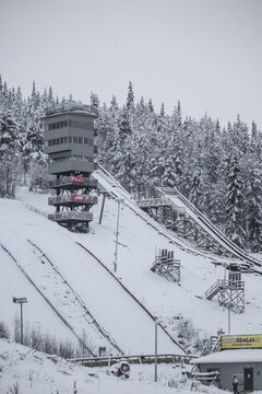View of snow-covered ski jump tower rising amidst the frosted forest, a stark contrast against the white landscape, hinting at winter sports adventure, Rovaniemi, Lapland, Finland.