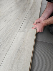 Person installs light wood flooring in a room with gray tile concept