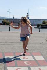 Cute girl playing hopscotch on playground outdoors. Little child playing hopscotch. Active child jumping on playground
