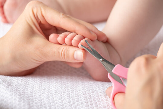 A caregiver trims a baby's tiny toe nails with pink scissors, emphasizing safe, gentle grooming and careful infant care in a calm, intimate moment