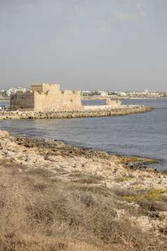 View of an old stone fortress standing defiant against the crashing waves, with the rugged coastline providing a stark contrast to the calm sea, Paphos, Paphos, Cyprus.