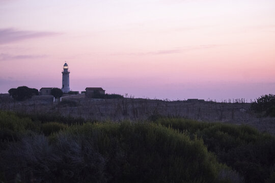 View of a solitary lighthouse standing tall against the soft, pastel hues of the twilight sky, casting a serene glow over the rugged landscape, Paphos, Paphos, Cyprus.