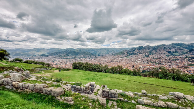 Aerial view of ancient stone ruins stand in stark contrast to the sprawling city nestled beneath a dramatic sky, a blend of history and modernity, Cusco, Peru.