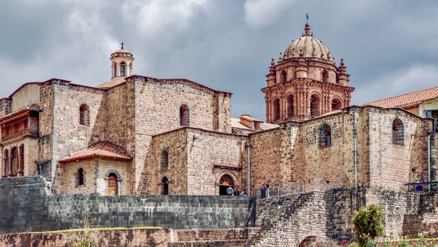 Aerial view of the Santo Domingo Convent's weathered stone walls and baroque dome rise against a dramatic sky, blending history and artistry, Cusco, Peru.