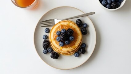 Stacked golden pancakes, fresh blueberries, blackberries, syrup