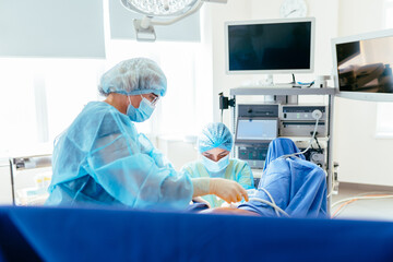 Female operating room nurse organizes surgical lines and medical equipment beside patient table during gynecological procedure. Sterile environment, controlled workflow, attention to detail