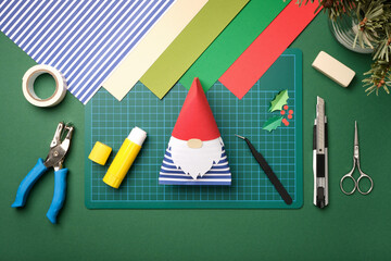 Paper gnome craft lies on desk for DIY projects. Around it are tools for art. Scissors, knife, glue, eraser, cutting mat.