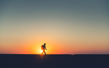 Man traveler with backpack walks along railway tracks at sunrise
