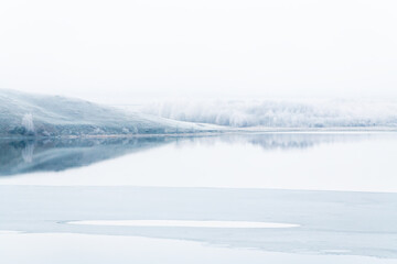 Mountains and frosted trees are reflected in the lake. Beautiful winter landscape