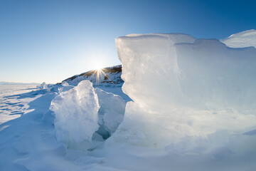 Blue transparent ice with snow on Baikal lake at sunset. Baikal, Russia.