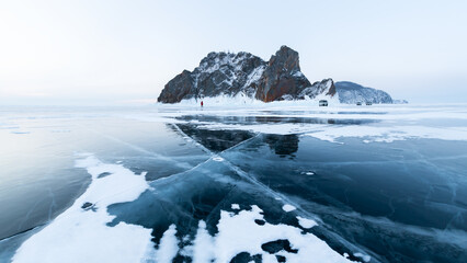 Blue transparent cracked ice with snow on Baikal lake in winter. Khoboy cape of Olkhon island, Baikal, Russia