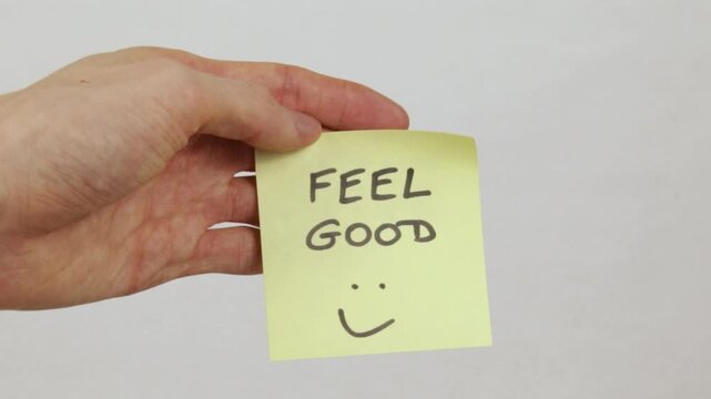 hand holding up sticky note with written text "FEEL GOOD" and a smily isolated on white or transparent png