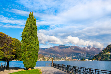 Beautiful view of Como lake, Italy. Promenade with trees in Como town. Clouds over the Alps mountains.
