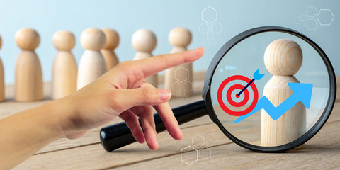 Abstract business background. A hand pointing to grab a magnifying glass focused on a wooden figure with the concept of targeting personnel selection for future business development.