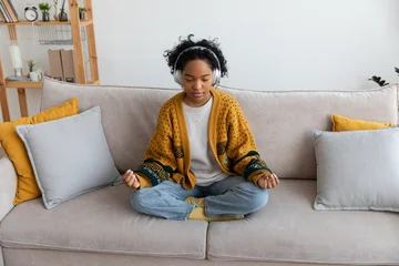 Fototapete Rund Lotusblume Yoga mindfulness meditation. Young healthy African girl practicing yoga at home. Woman sitting in lotus pose on couch meditating smiling relaxing indoor. Girl doing breathing practice. Yoga at home  © Юлия Завалишина