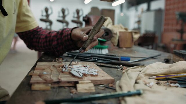 Close up of a carpenter using a chisel and mallet to carefully carve an intricate design into a wooden plank in a workshop, Siem Reap, Cambodia.