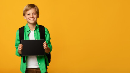 Happy teenager blond boy, caucasian pupil show tablet with empty screen, isolated on orange background, panorama. Back to school with device, online lesson and education remote, great website, app