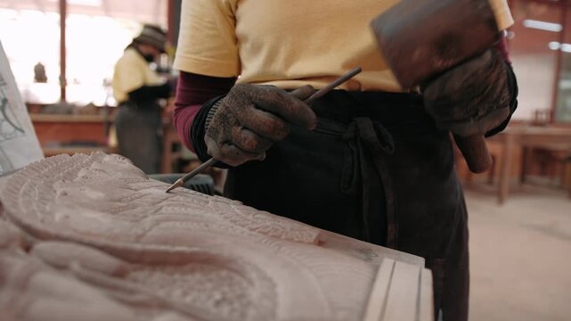 Close up of a craftsman create an intricate stone bas relief using a chisel and mallet. Siem Reap, Cambodia.
