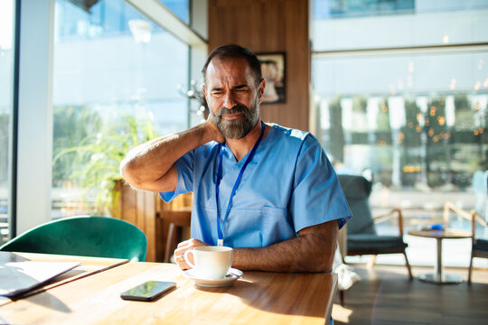 Adult healthcare worker grimacing with neck pain in hospital cafe