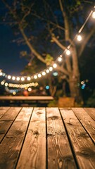 Wood planks lead to blurred scene warm outdoor lights strung in trees above tables at night