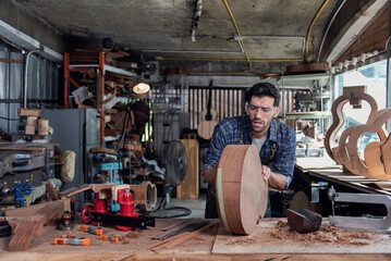 Woodworker in apron sanding the edge of guitar body using manual tool with sanding paper.