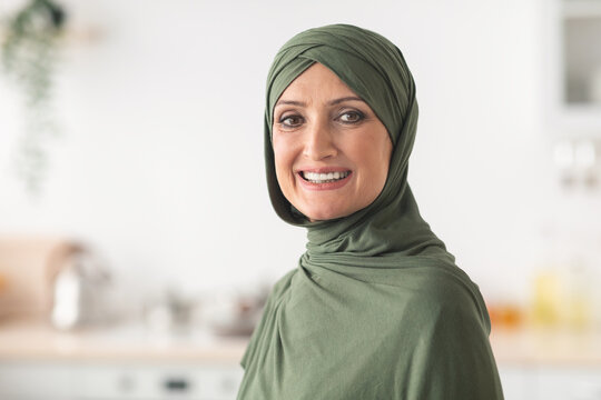 Portrait Of Happy Mature Muslim Lady Wearing Hijab Standing In Kitchen At Home. Modern Middle-Eastern Housewife Posing Indoors, Smiling To Camera. Headshot Of Beautiful Arab Female