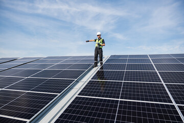 Technician installing solar panels on factory roof for green energy. A skilled technician in safety gear is working on a solar panel installation on rooftop.